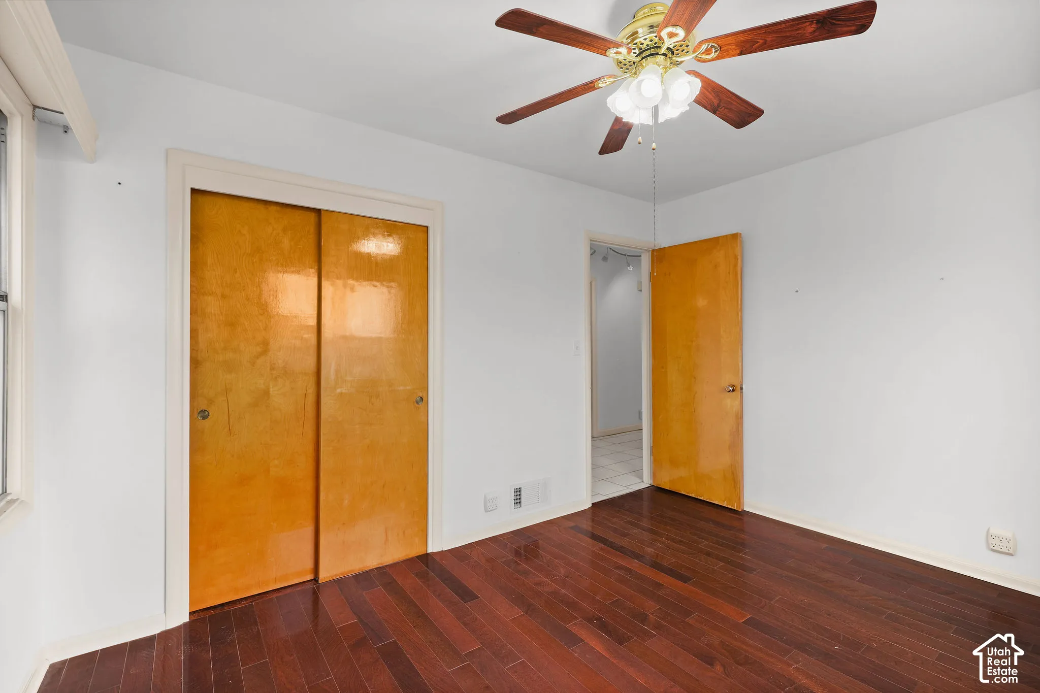 Dark wood-finish flooring, bright white walls, a ceiling fan with integrated lighting, and a window with white trim