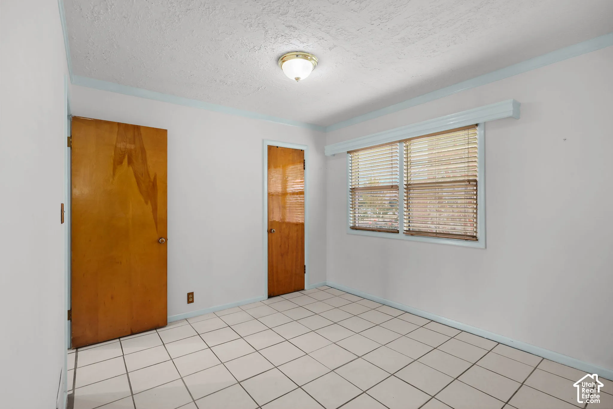 Room featuring square tile flooring, wood-finish doors, a window with horizontal blinds, and a flush-mount ceiling light fixture