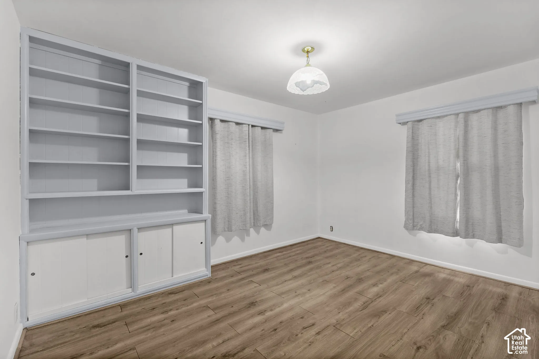 Wood-finish flooring, built-in shelving, built-in storage cabinets, window treatments, and a ceiling-mounted light fixture