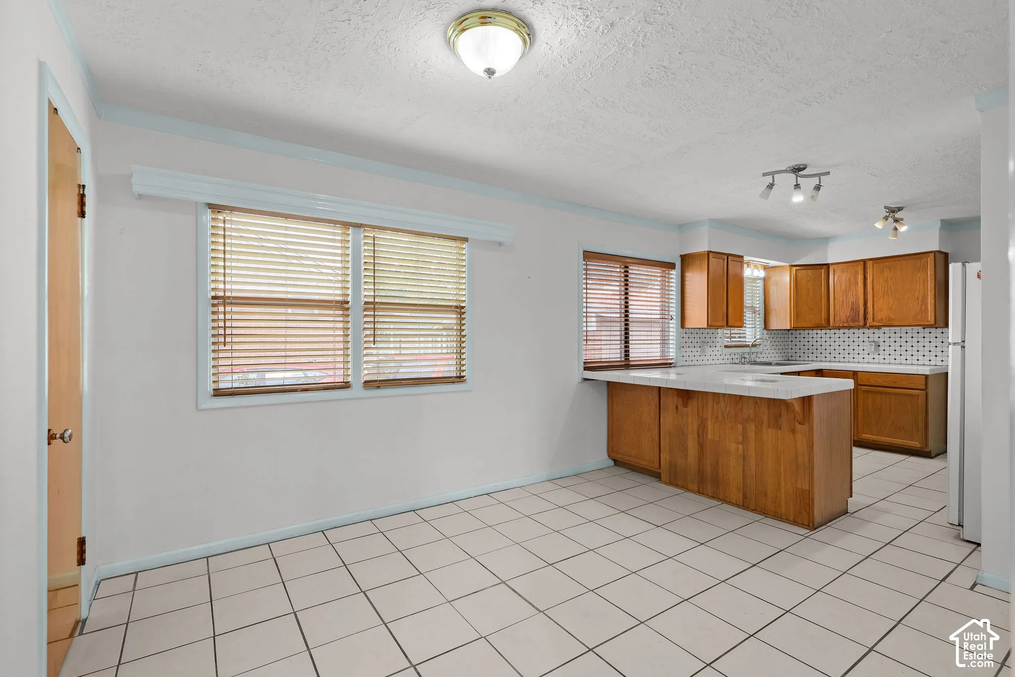 White tile flooring, wood cabinetry, track lighting, and a white tile backsplash