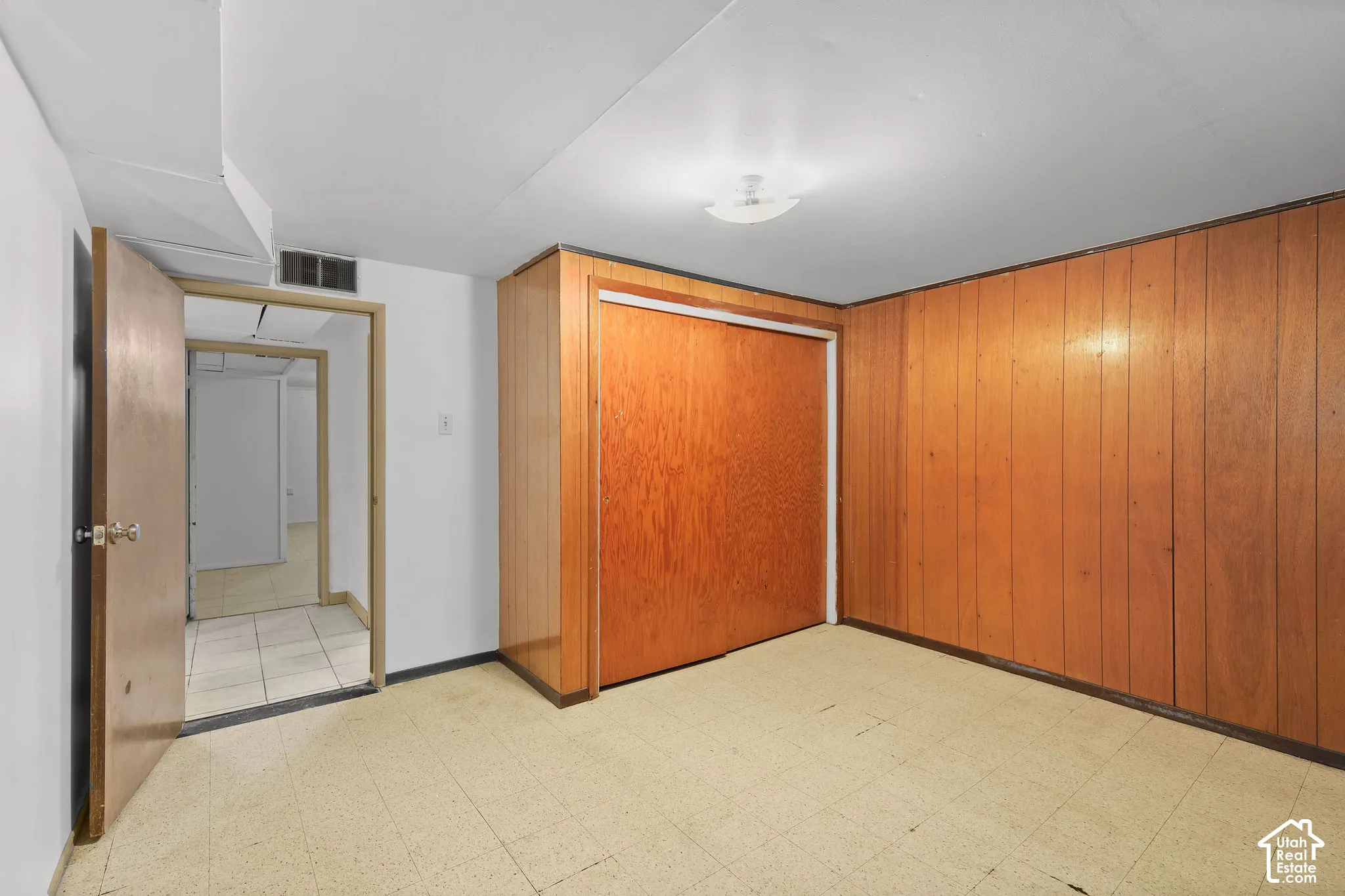 Wall-to-wall wood paneling, wood-finish sliding closet doors, white painted walls, and ceiling-mounted flush light fixture