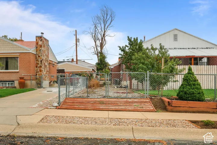 Chain-link fence enclosing a paved area with a raised wood-finish planter and compact evergreen shrub