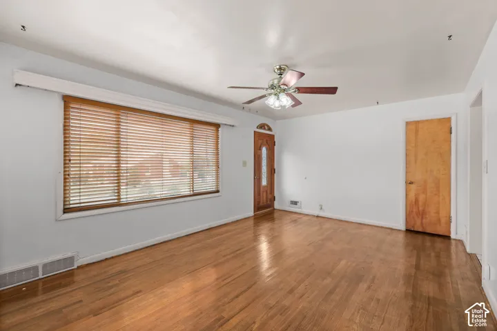 Hardwood flooring, wood-finish blinds, wood entry door with glass insert, wood interior door, and a ceiling fan with integrated lighting