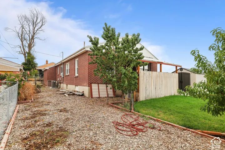 Brick exterior with a covered patio structure, a privacy fence, and an outdoor storage shed