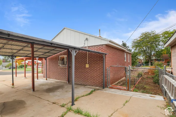 Brick exterior building with white siding, covered carport, concrete driveway, and chain-link fence