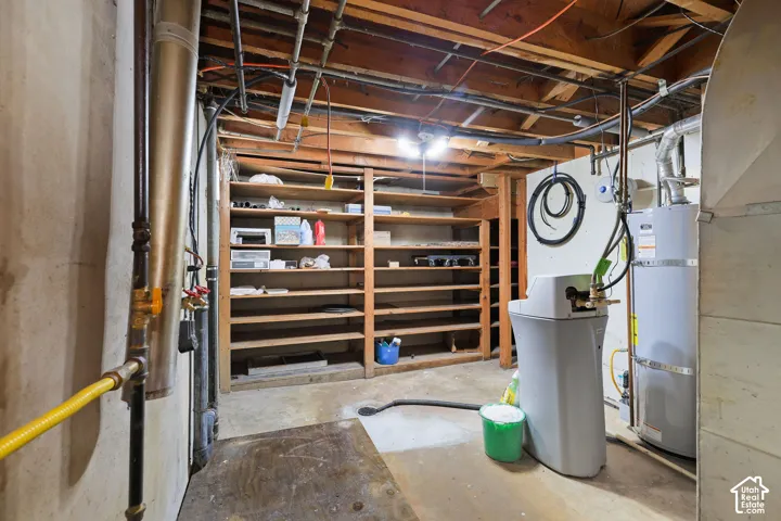 Basement utility area featuring exposed joists, built-in shelving, a water heater, and a water softener