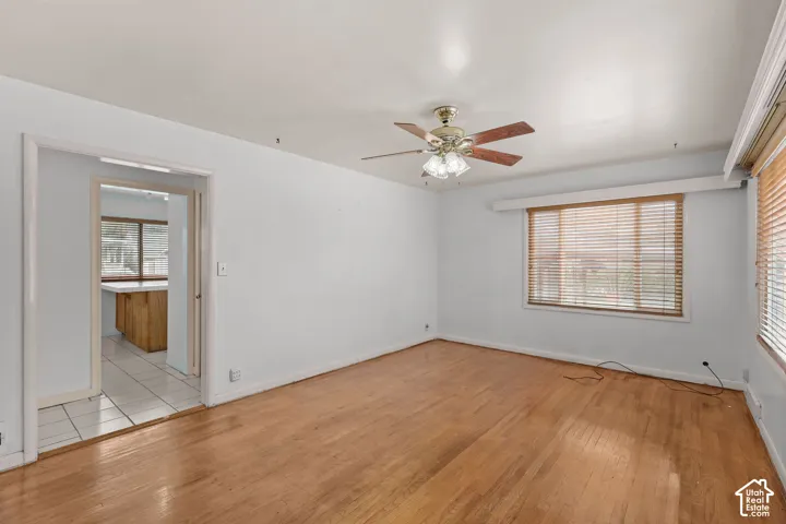 Hardwood flooring, ceiling fan with light fixture, large window with blinds, and a doorway to a tiled area