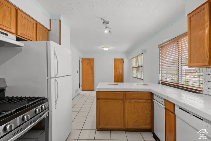 Kitchen featuring light wood cabinetry, white tile countertops, tile flooring, and white appliances