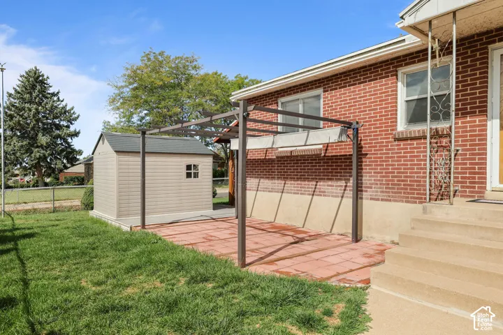 Red brick exterior, concrete steps, attached patio cover, patio pavers, and a freestanding storage shed