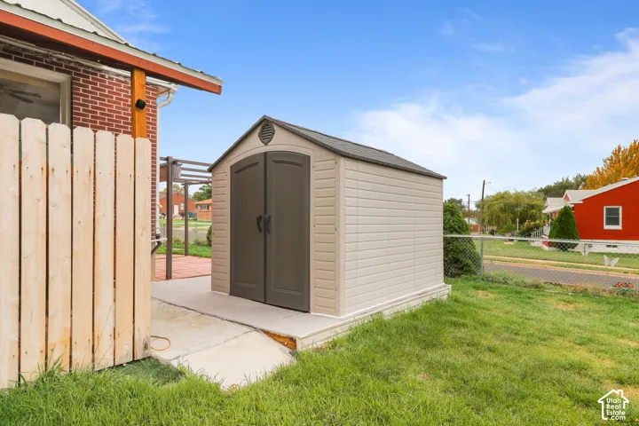 Detached storage shed with double doors, set on a concrete pad, alongside a wooden privacy fence, and a brick exterior building