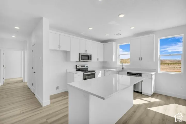 Kitchen featuring white cabinetry, a central island, stainless steel appliances, and wood-finish flooring