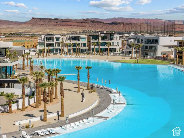 Expansive lagoon-style pool with sandy shoreline, surrounding modern multi-story residences, and mature palm trees