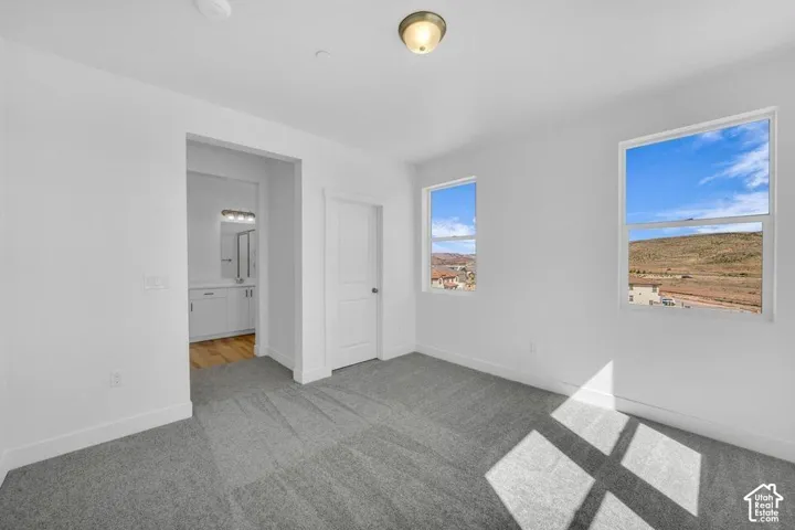 Plush grey carpeting, white interior walls, overhead flush mount lighting, and two windows providing expansive outdoor scenery