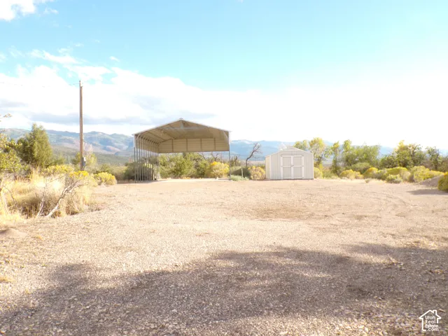 Gravel lot featuring a metal carport and a storage shed, with a prominent mountain backdrop