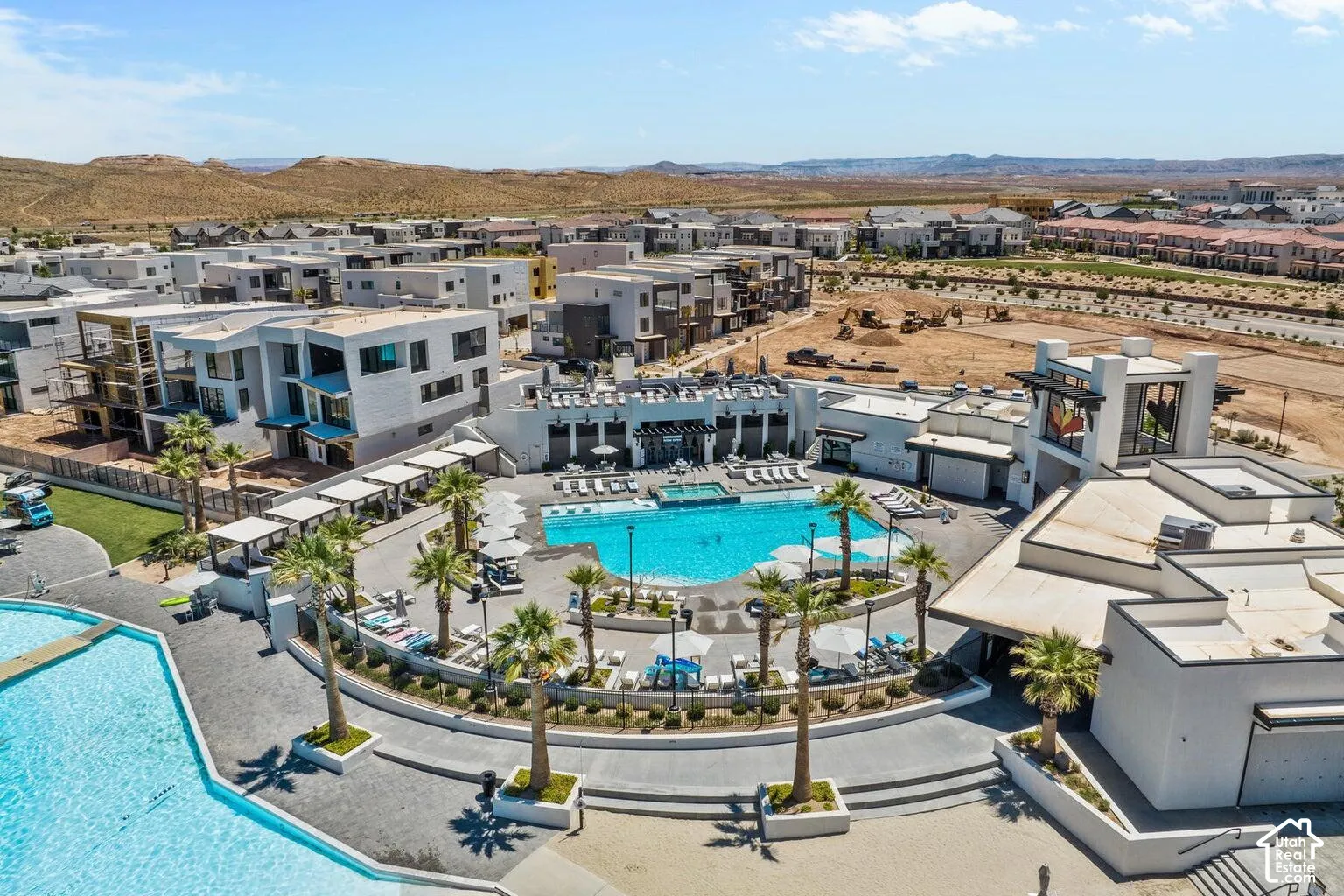 Community pool area featuring multiple swimming pools, surrounding lounge seating, mature palm trees, and modern building architecture