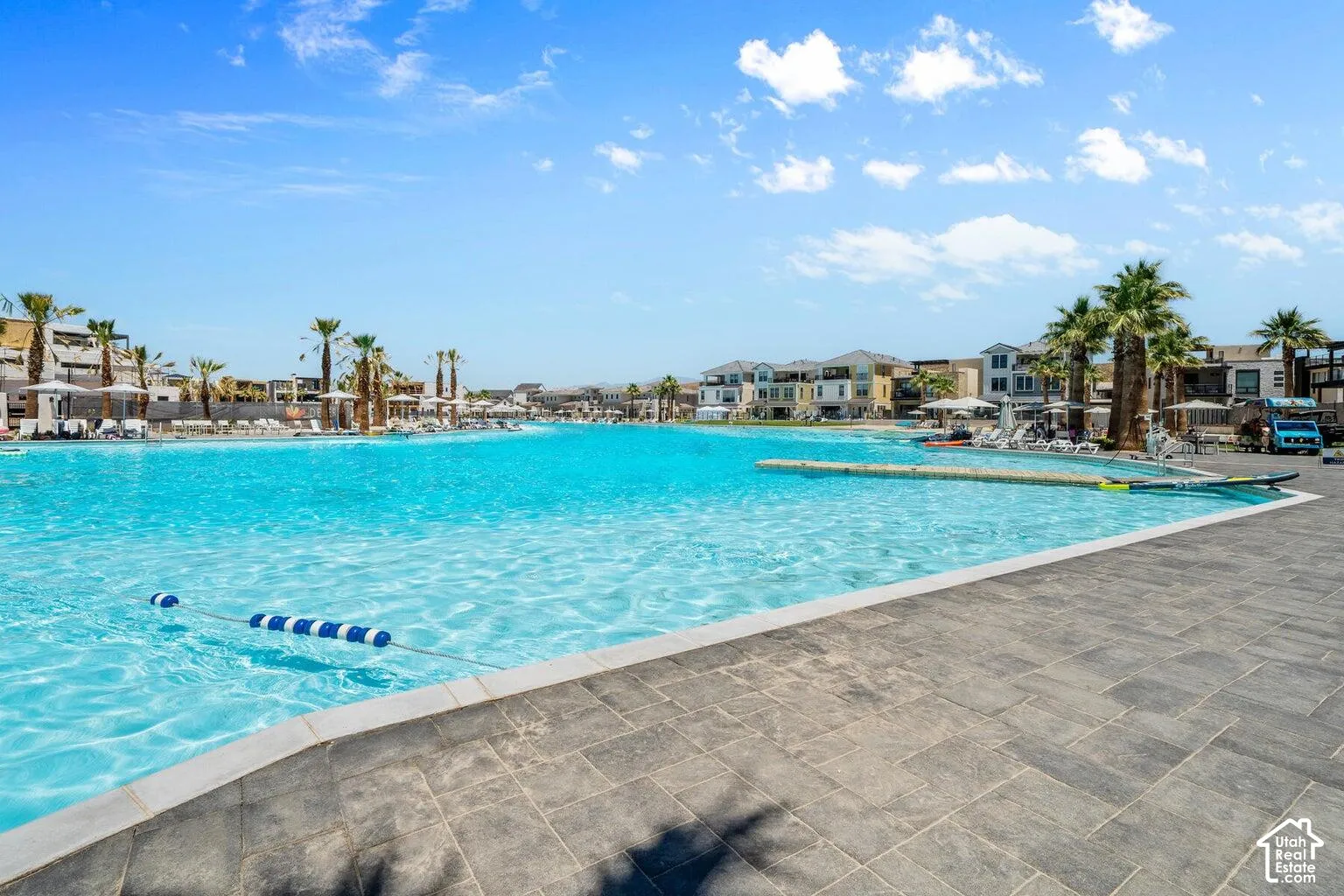 Expansive artificial lagoon with bright blue water, surrounded by paved hardscaping and mature palm trees