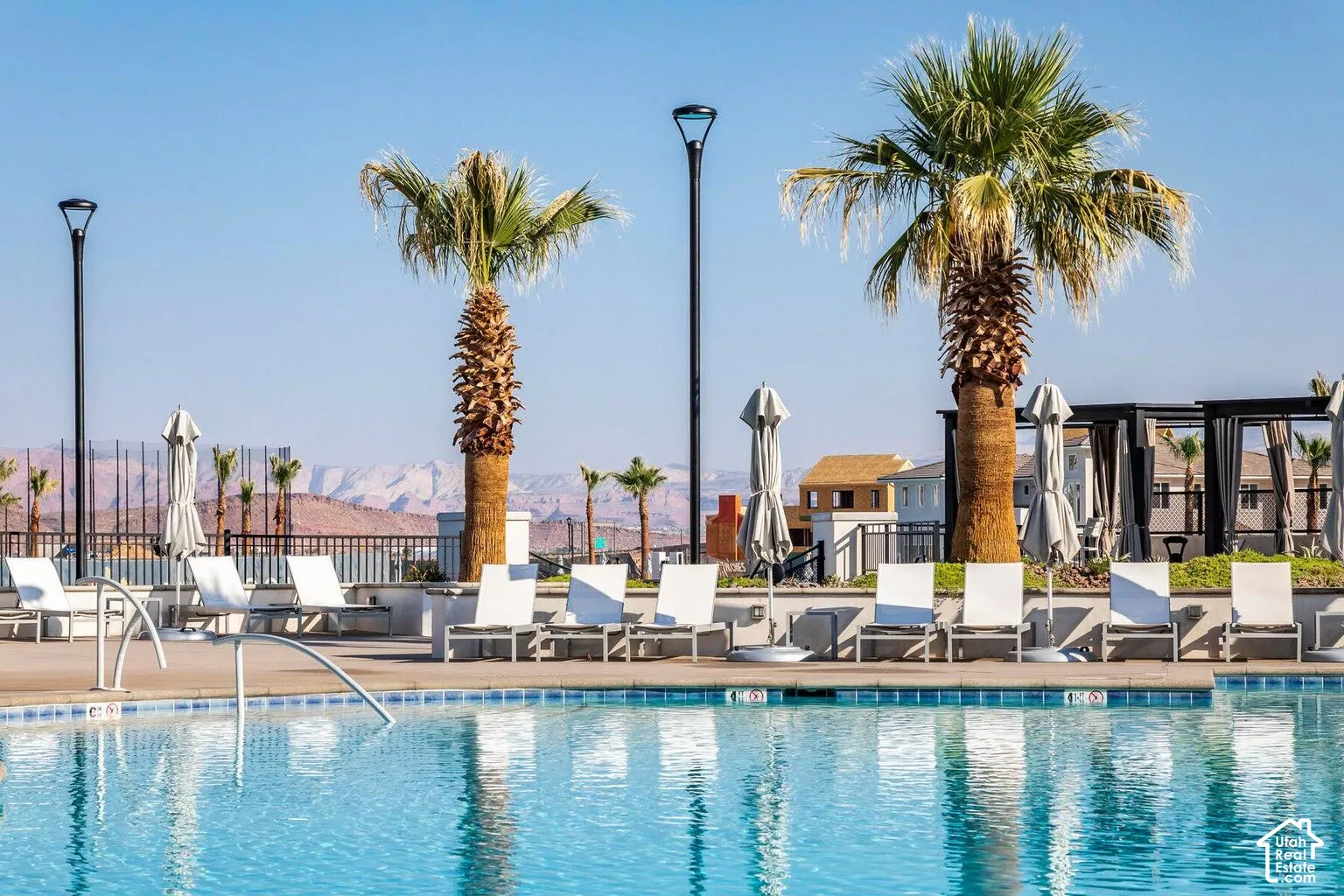 Sparkling swimming pool with a tiled edge, surrounded by a paved deck, mature palm trees, and mountain scenery