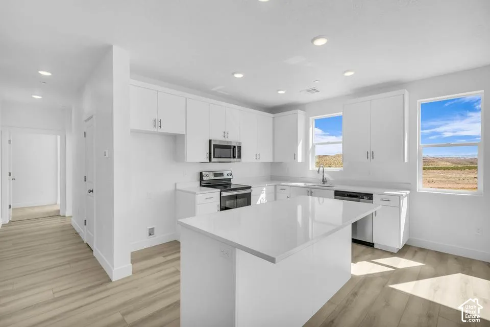 White shaker cabinetry, recessed lighting, wood-finish flooring, a kitchen island, and stainless steel appliances
