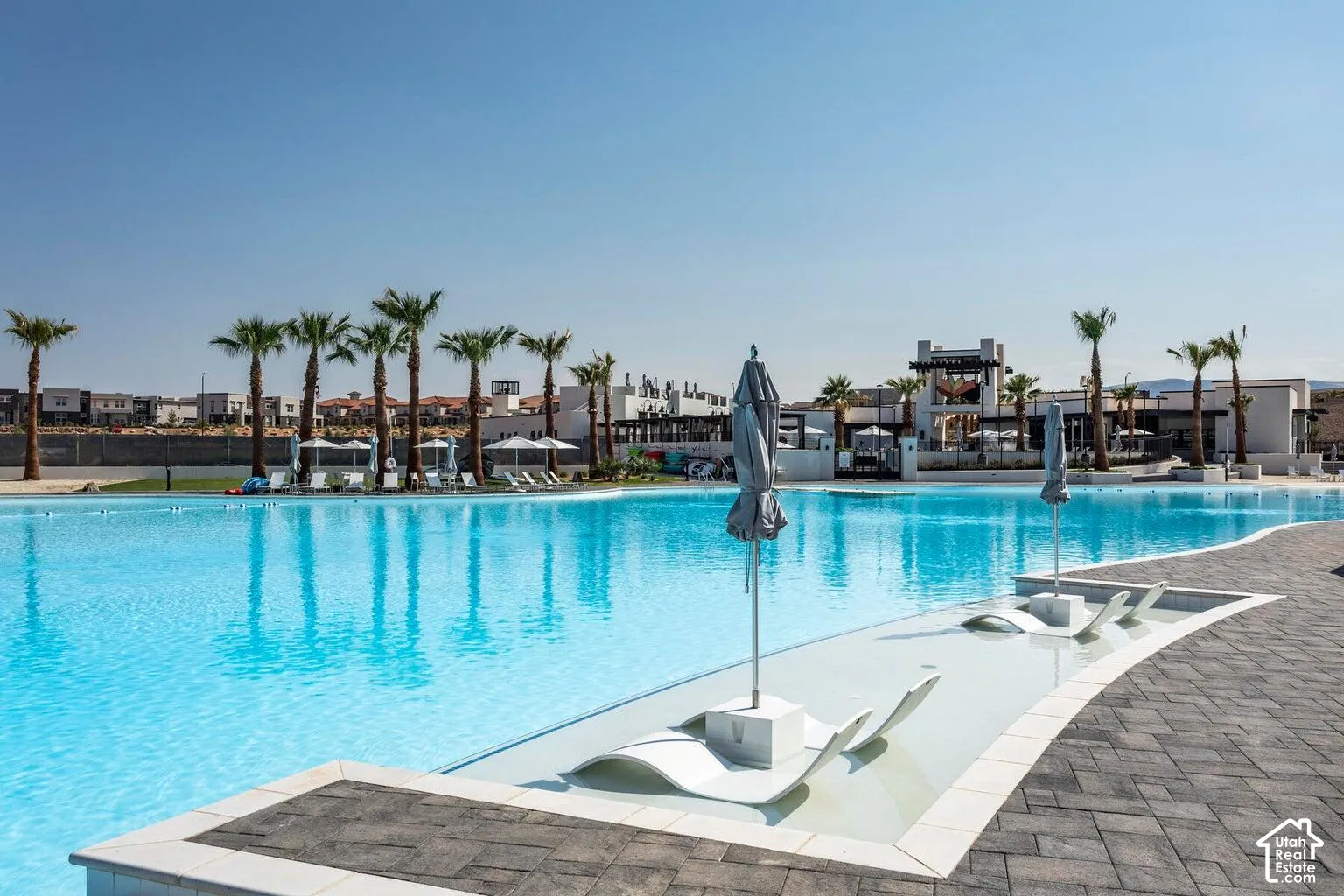 Expansive blue-bottomed lagoon with integrated lounging areas, surrounded by palm trees and paver hardscaping