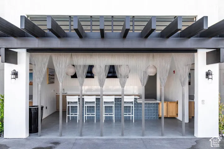 Outdoor kitchen with a slatted pergola, white countertops, blue tiled island, and built-in cabinetry