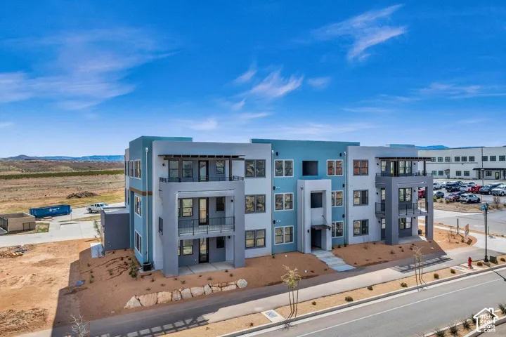 Modern multi-story building featuring balconies with glass railings, a flat roofline, and a multi-toned exterior finish