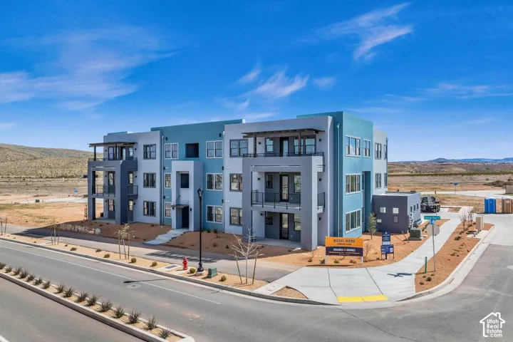 Contemporary multi-story building featuring multiple balconies, a varied blue and gray exterior, and a flat roofline