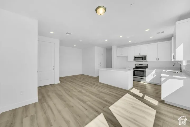 White shaker cabinetry, stainless steel appliances, wood-finish flooring, recessed lighting, and a kitchen island