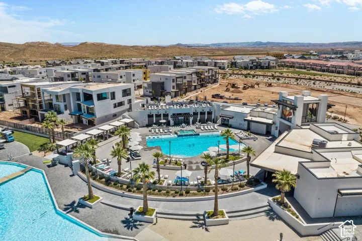 Community pool area featuring multiple swimming pools, surrounding lounge seating, mature palm trees, and modern building architecture