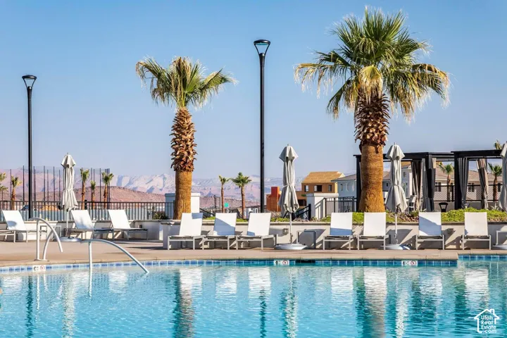 Sparkling swimming pool with a tiled edge, surrounded by a paved deck, mature palm trees, and mountain scenery