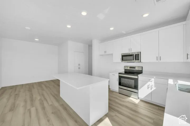 Modern kitchen with white cabinetry, light countertops, stainless steel appliances, and wood-finish flooring