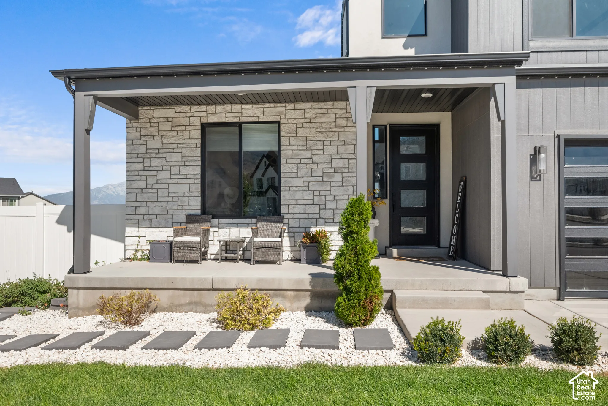 Modern exterior featuring a prominent covered porch, stone veneer accents, vertical siding, a contemporary entry door with frosted glass panels, and a concrete pathway with stepping stones