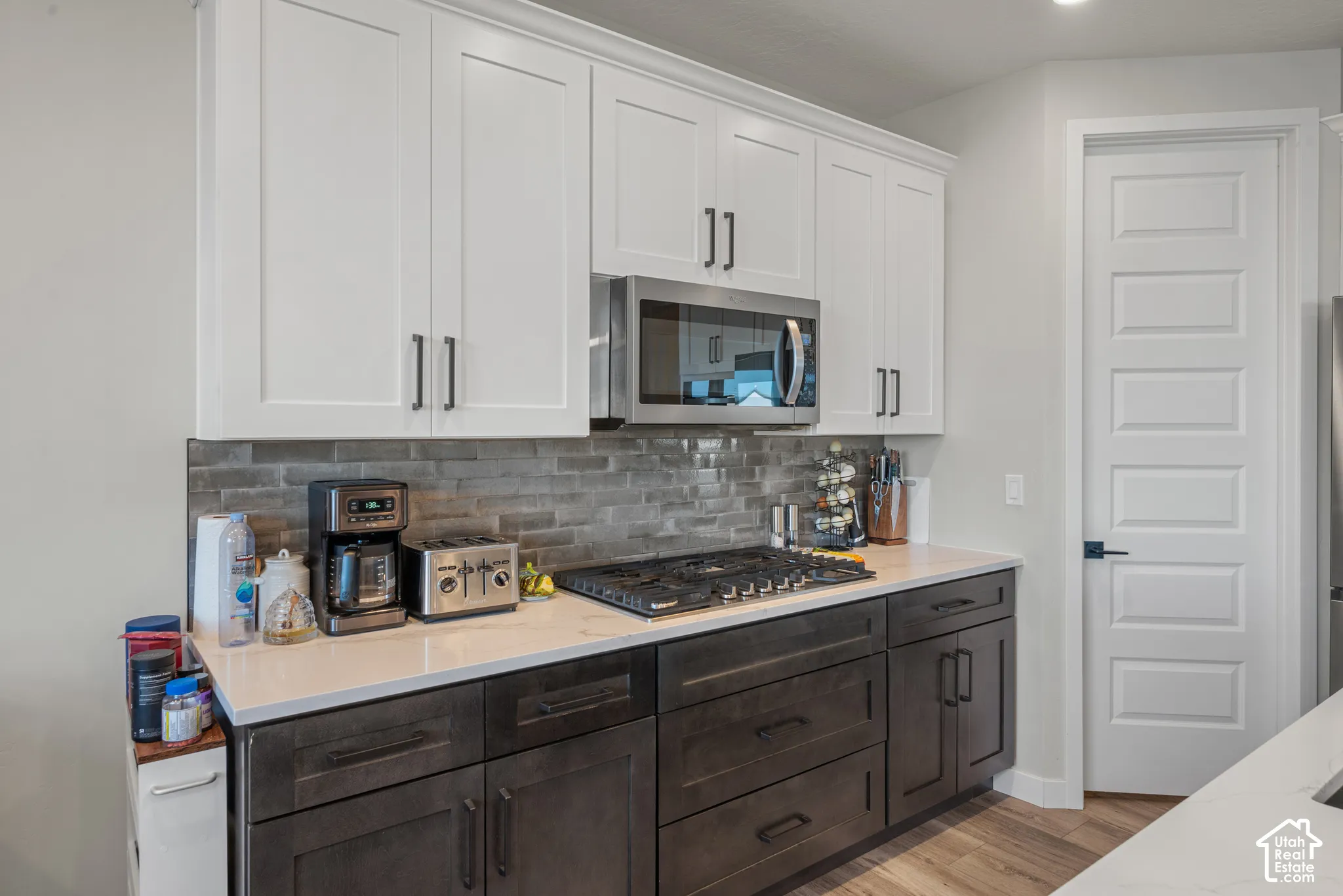 Kitchen featuring white upper cabinetry, dark lower cabinetry, light-colored countertops, a tile backsplash, and a built-in microwave