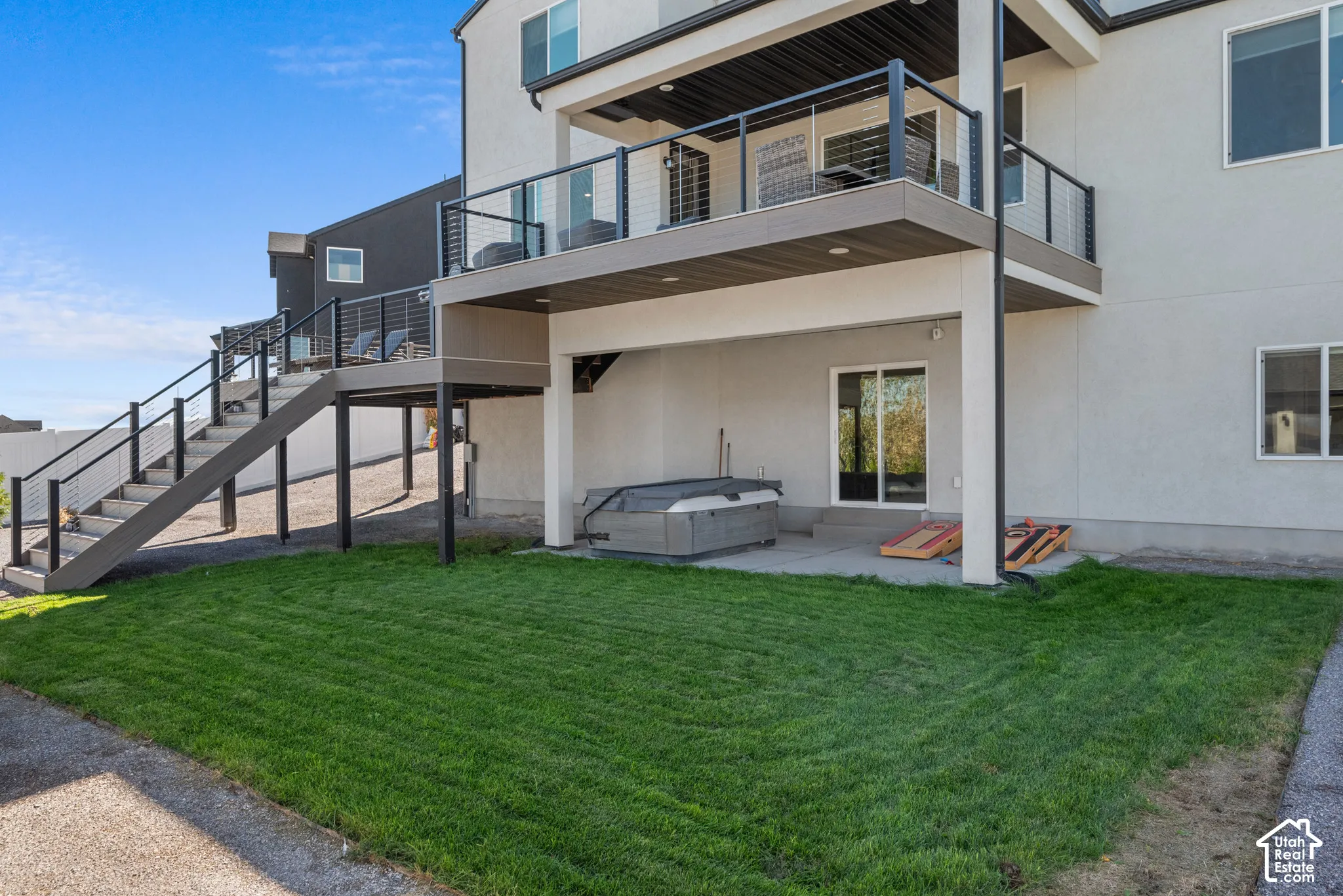 Upper-level deck with cable railing, ground-level patio, and a grass area