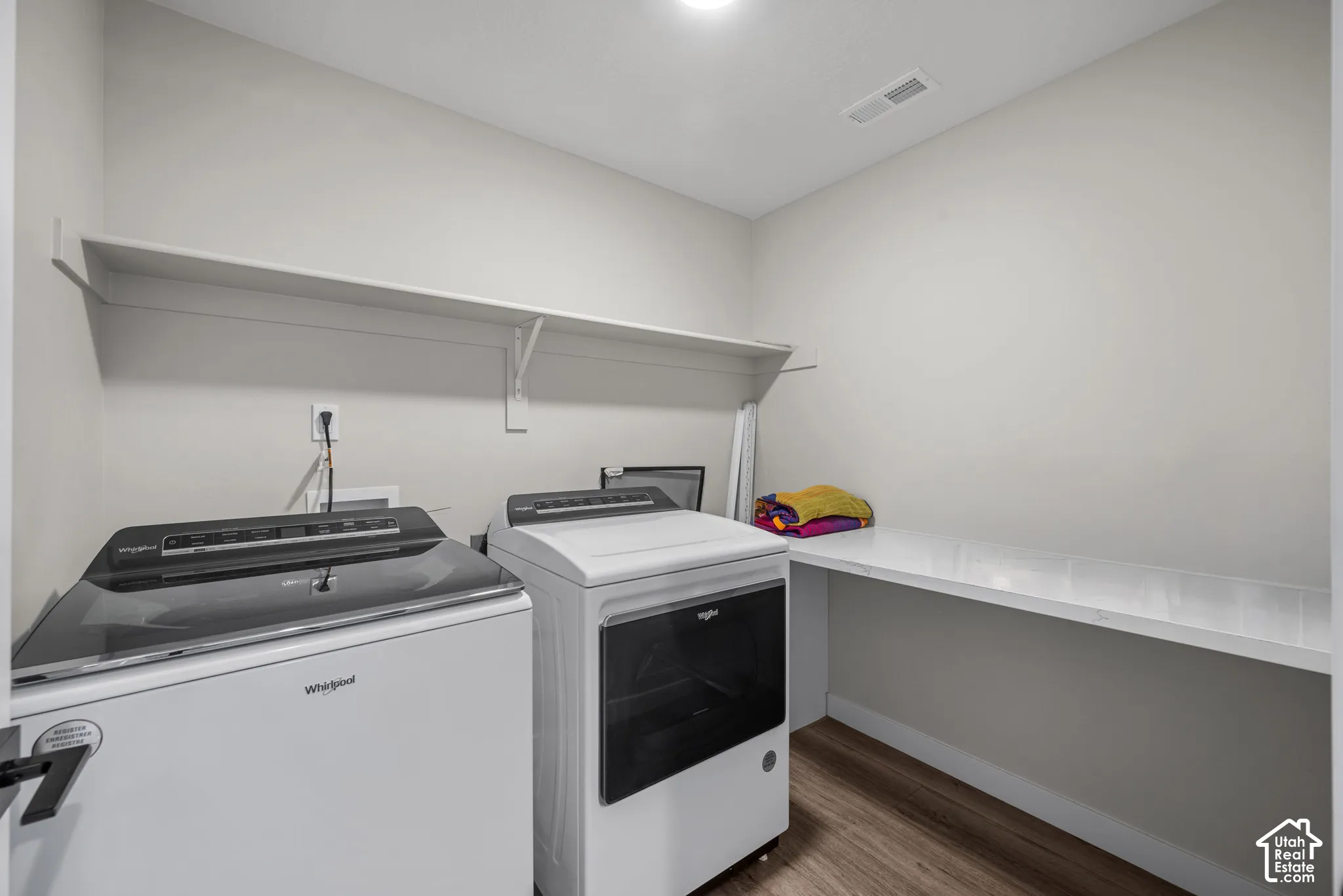 Utility room featuring wood-finish flooring, a built-in countertop, and an overhead shelf