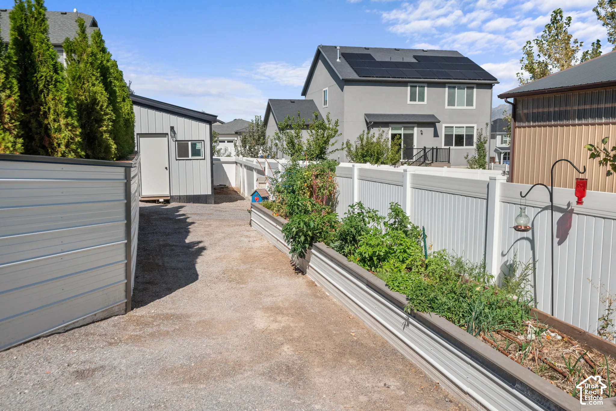 Raised garden beds, gravel pathway, vinyl fencing, and a detached shed with a single window