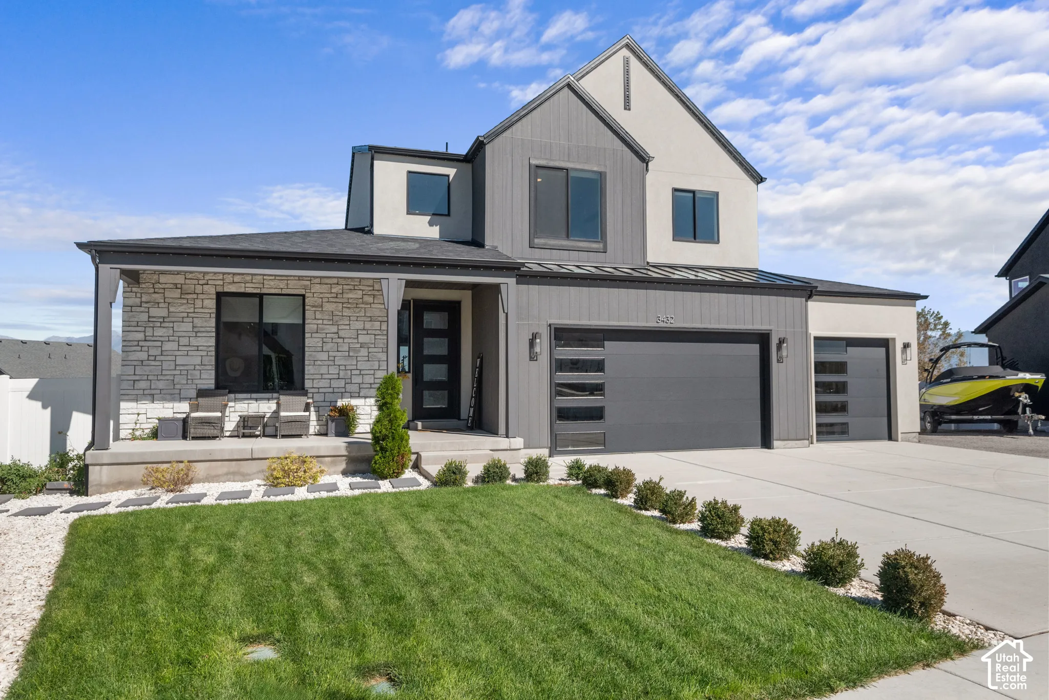 Modern exterior featuring stone veneer, covered porch, multi-panel garage doors, and a concrete driveway