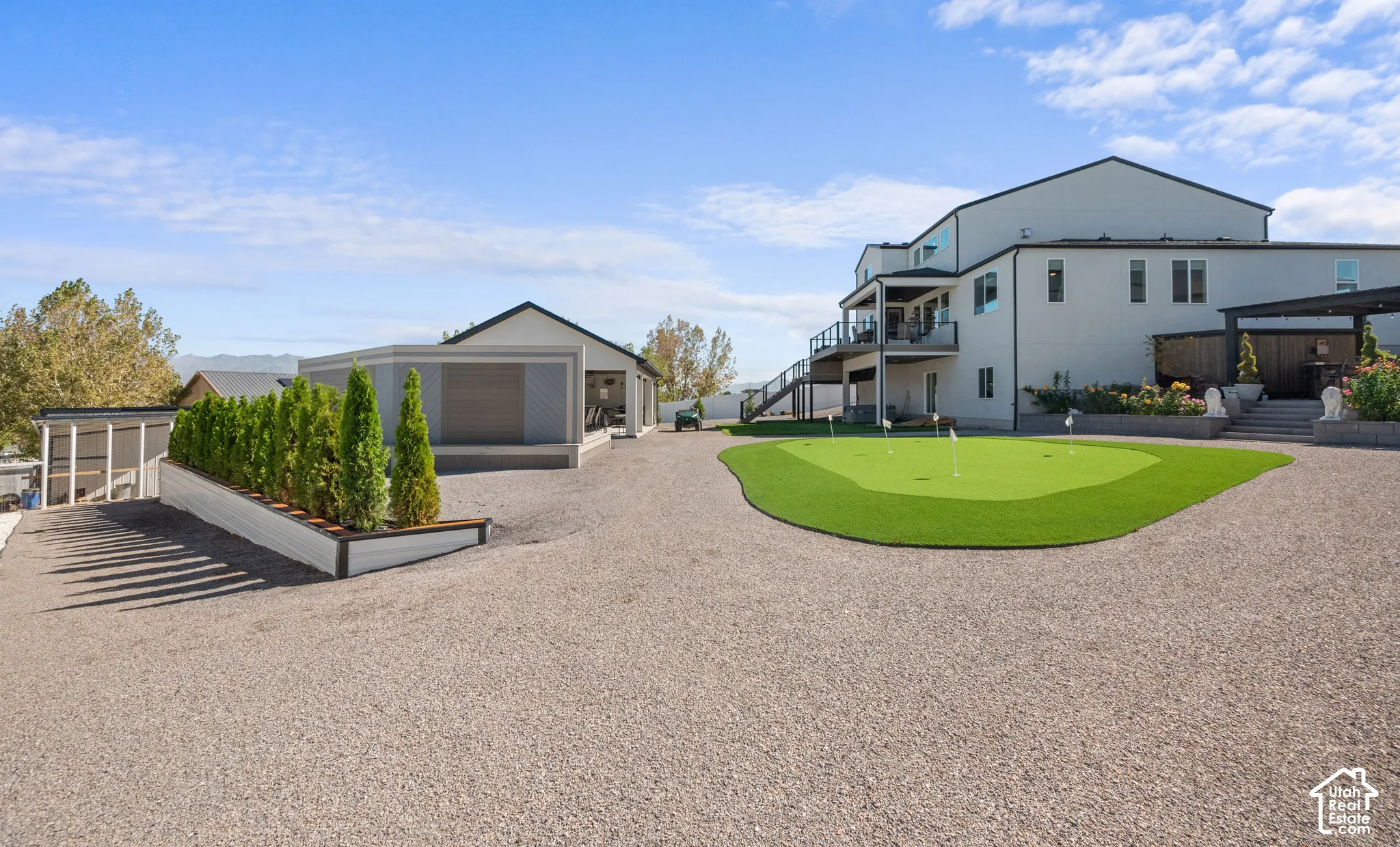 Expansive gravel driveway, artificial turf putting green, multiple-story exterior, upper-level balcony, and covered outdoor structure