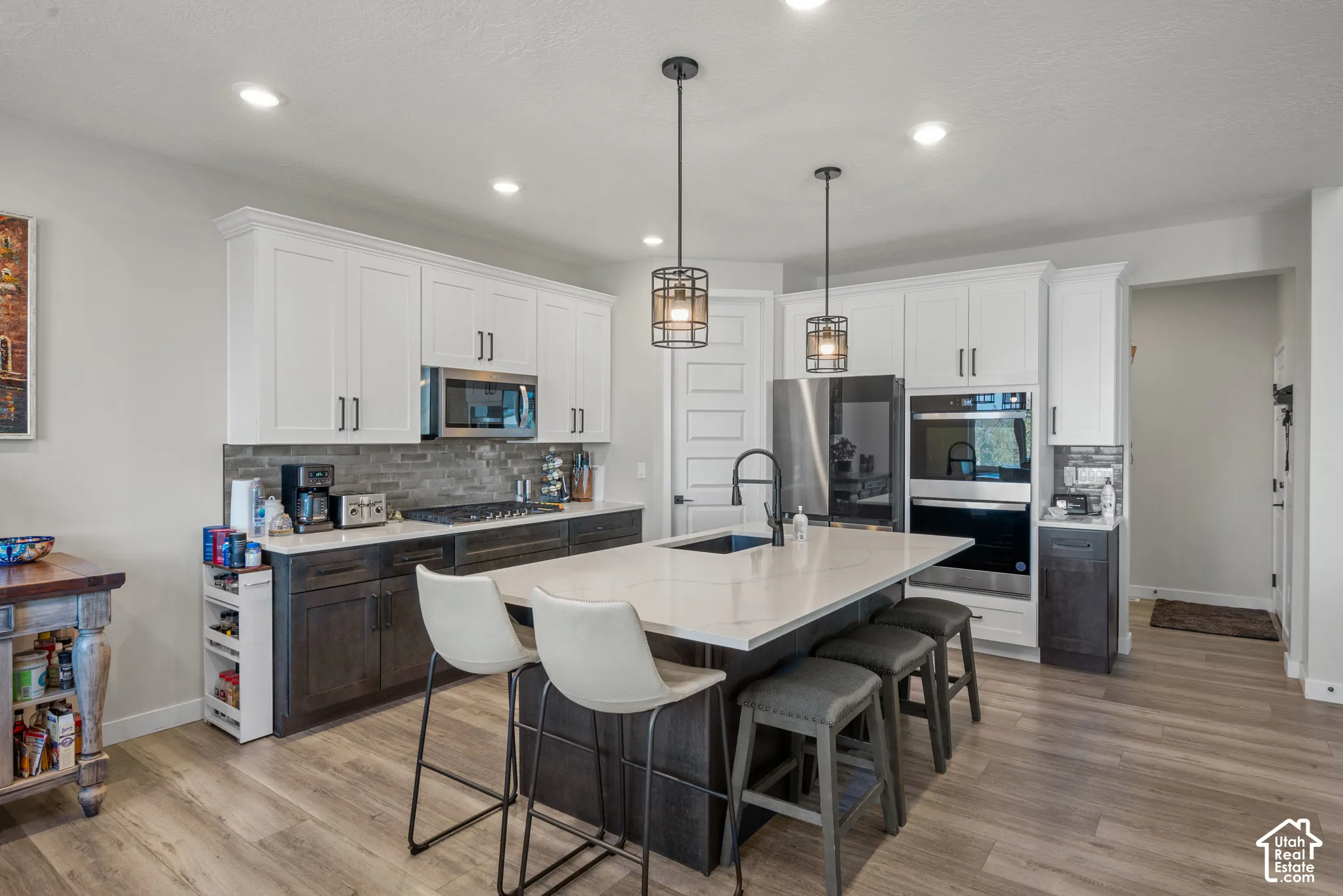 Gourmet kitchen featuring white upper cabinetry, dark wood-finish lower cabinetry, stone-finish backsplash, stainless steel appliances, and a central island with countertop seating