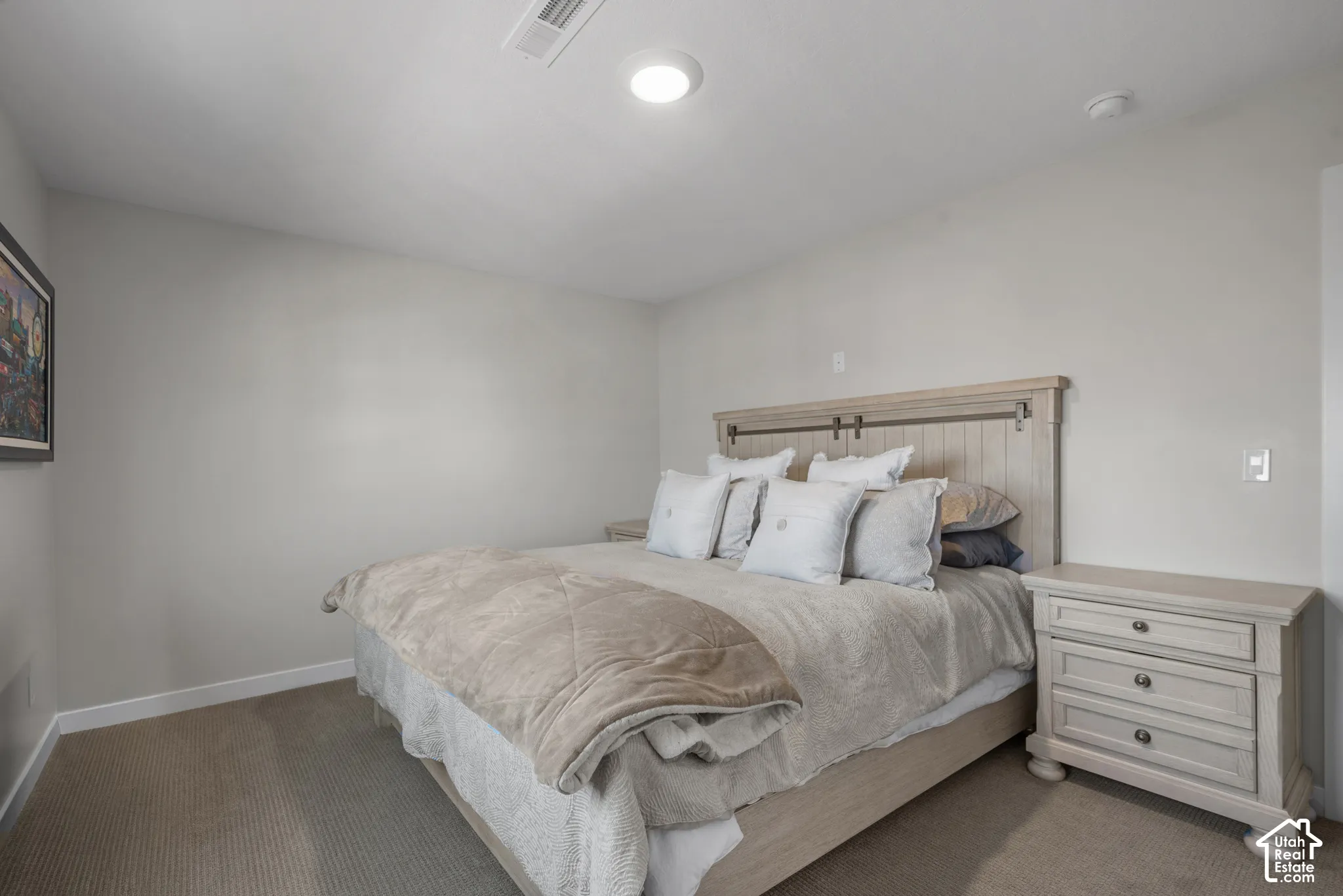 Carpeted room featuring a light-colored wood headboard with barn door detailing, recessed ceiling light, and a matching wood nightstand with three drawers