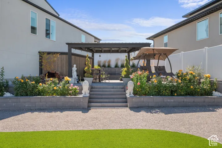 Landscaped backyard featuring a dark pergola, tiered retaining walls, and a white privacy fence