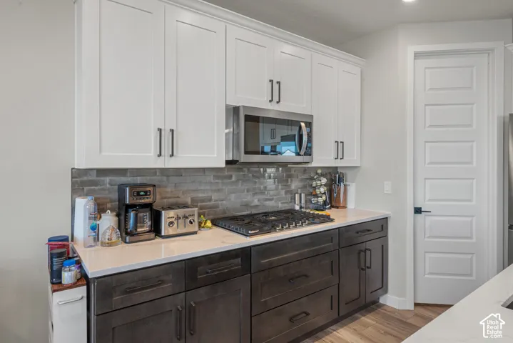 Kitchen featuring white upper cabinetry, dark lower cabinetry, light-colored countertops, a tile backsplash, and a built-in microwave