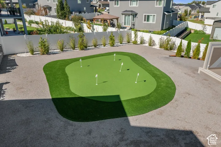 Private backyard putting green with multiple flags, surrounded by a gravel perimeter, and bordered by a white privacy fence