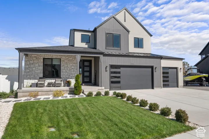 Modern exterior featuring stone veneer, covered porch, multi-panel garage doors, and a concrete driveway