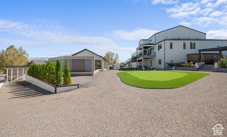 Expansive gravel driveway, artificial turf putting green, multiple-story exterior, upper-level balcony, and covered outdoor structure