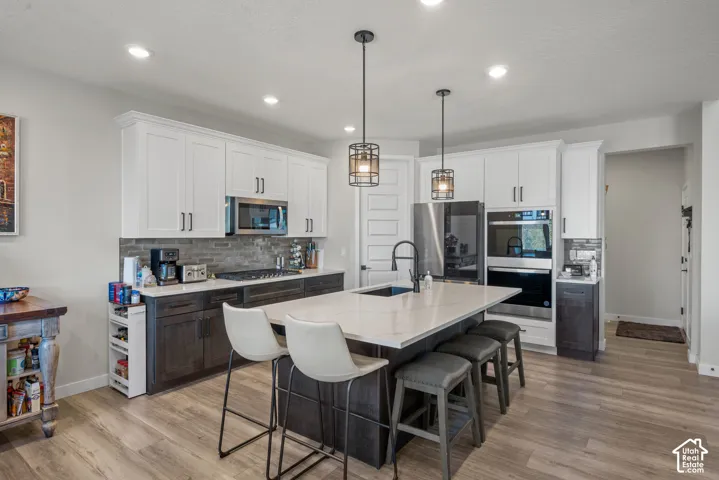 Gourmet kitchen featuring white upper cabinetry, dark wood-finish lower cabinetry, stone-finish backsplash, stainless steel appliances, and a central island with countertop seating