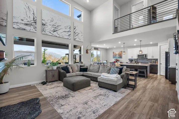 Expansive living area with high ceilings, large windows, wood-finish flooring, and a second-story interior balcony with metal railings