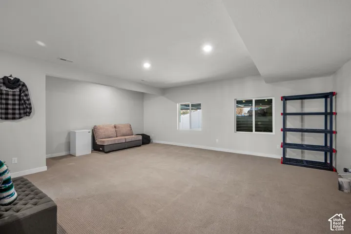 Recessed lighting illuminates a spacious room with light gray walls and neutral carpeting, featuring two windows