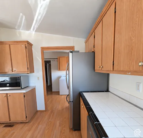 Kitchen featuring wood-finish cabinetry, white tile countertops, and stainless steel appliances