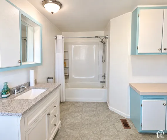 Vanity with integrated sink and granite-finish countertop, full bathtub and shower combination, gray tile-look flooring, and built-in cabinetry with light blue accents