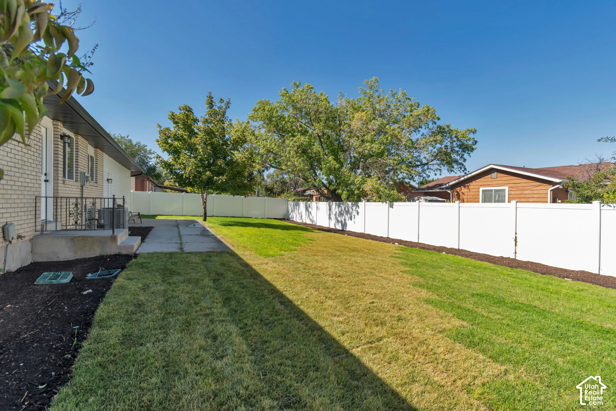 Expansive yard featuring a large grass area, mature trees, a white privacy fence, and a concrete patio with a wrought iron railing